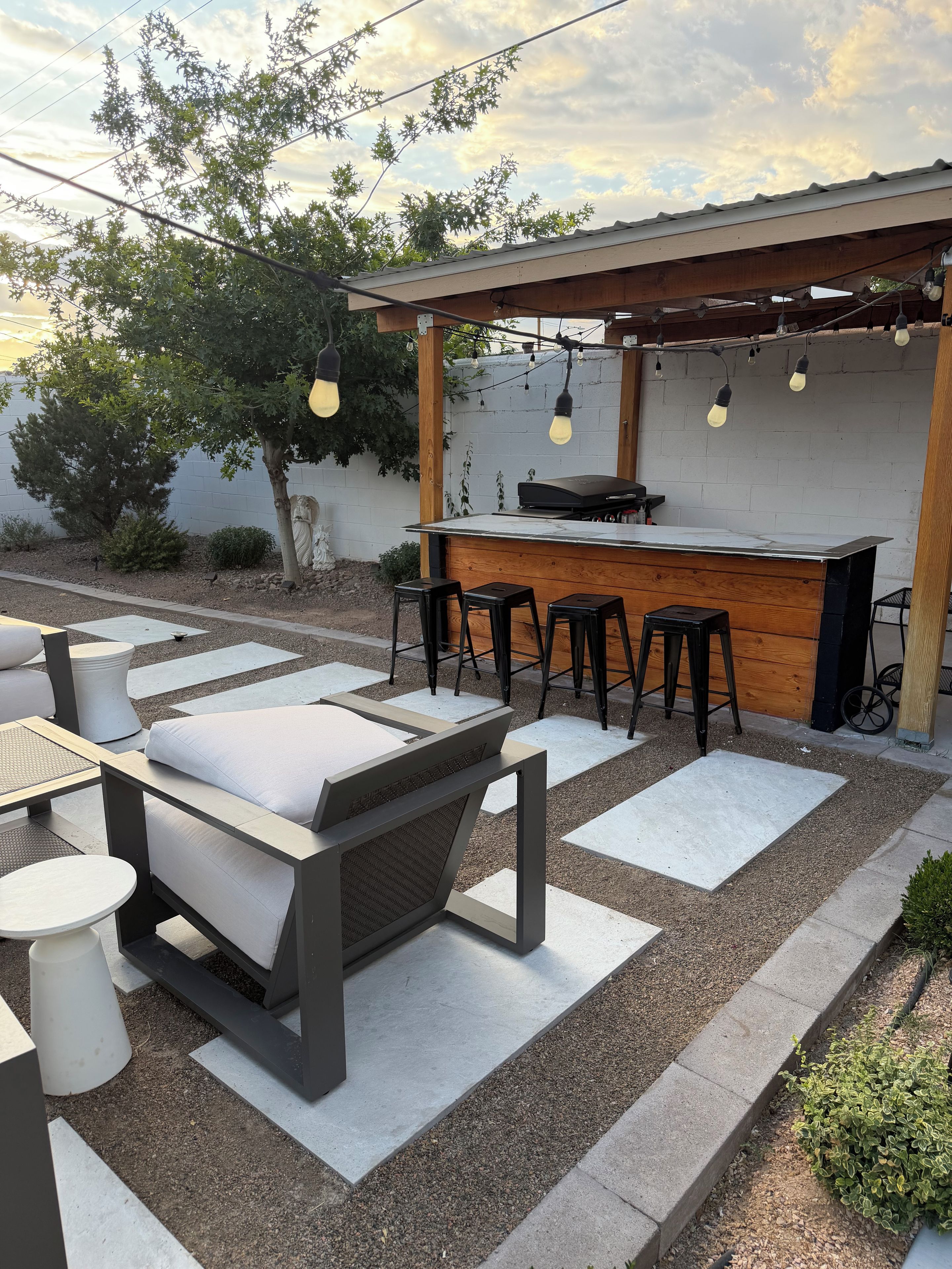 Une terrasse extérieure dotée d’un bar, de coins salon et d’une pergola illuminée de guirlandes lumineuses.