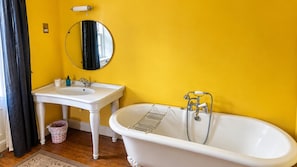 Un baño con una bañera blanca, un lavamanos y un espejo sobre una pared amarilla.