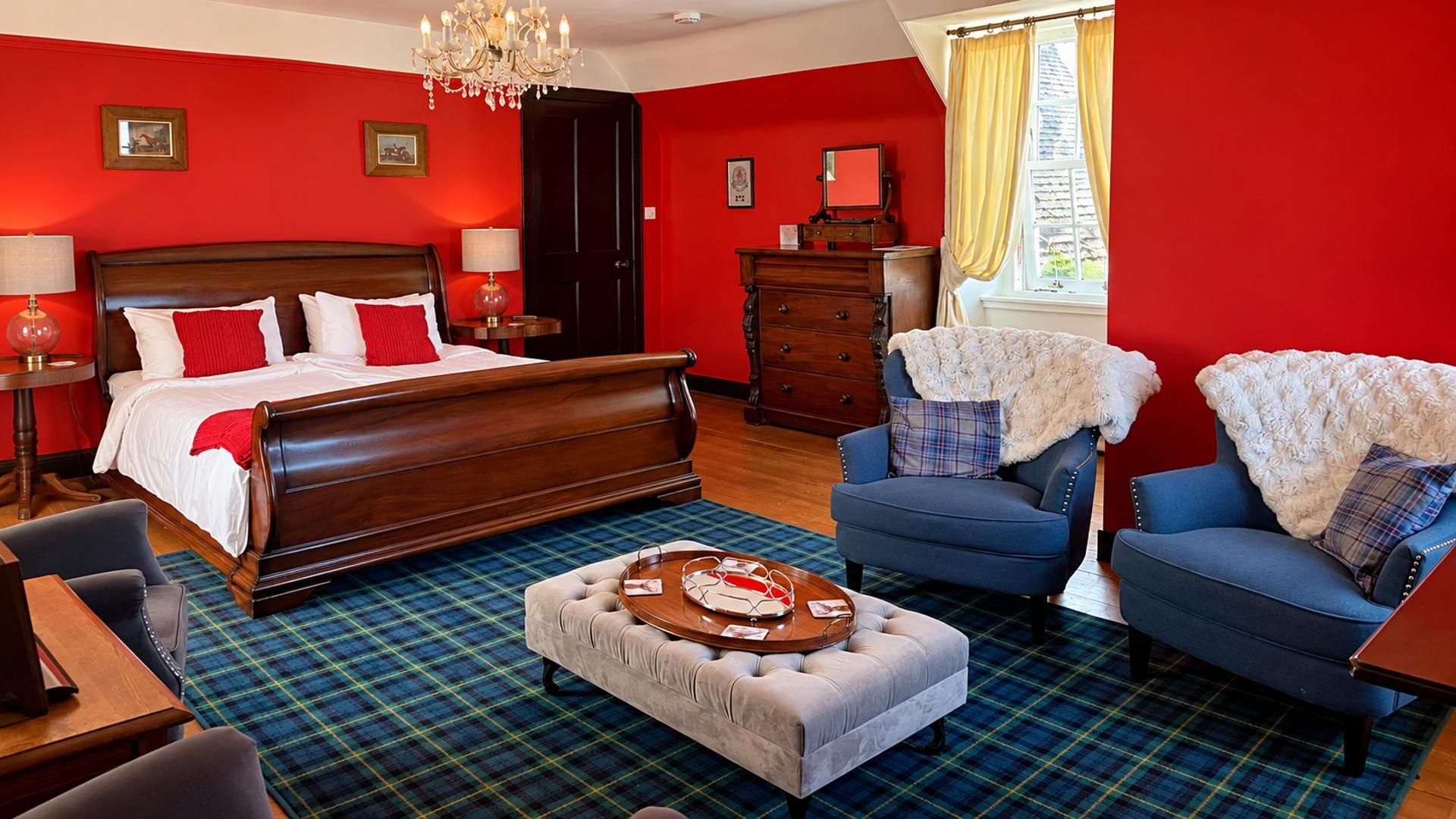 A hotel room with a large bed, two armchairs, a coffee table, a dresser, and a window with curtains.