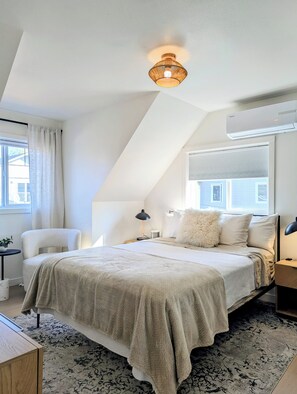 Quarto com cama, poltrona, mesa de cabeceira, abajur e luminária no teto.