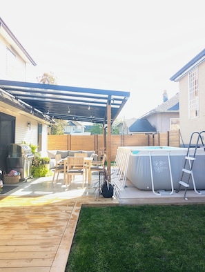 Ein Garten mit überdachter Terrasse, Whirlpool und Grill.