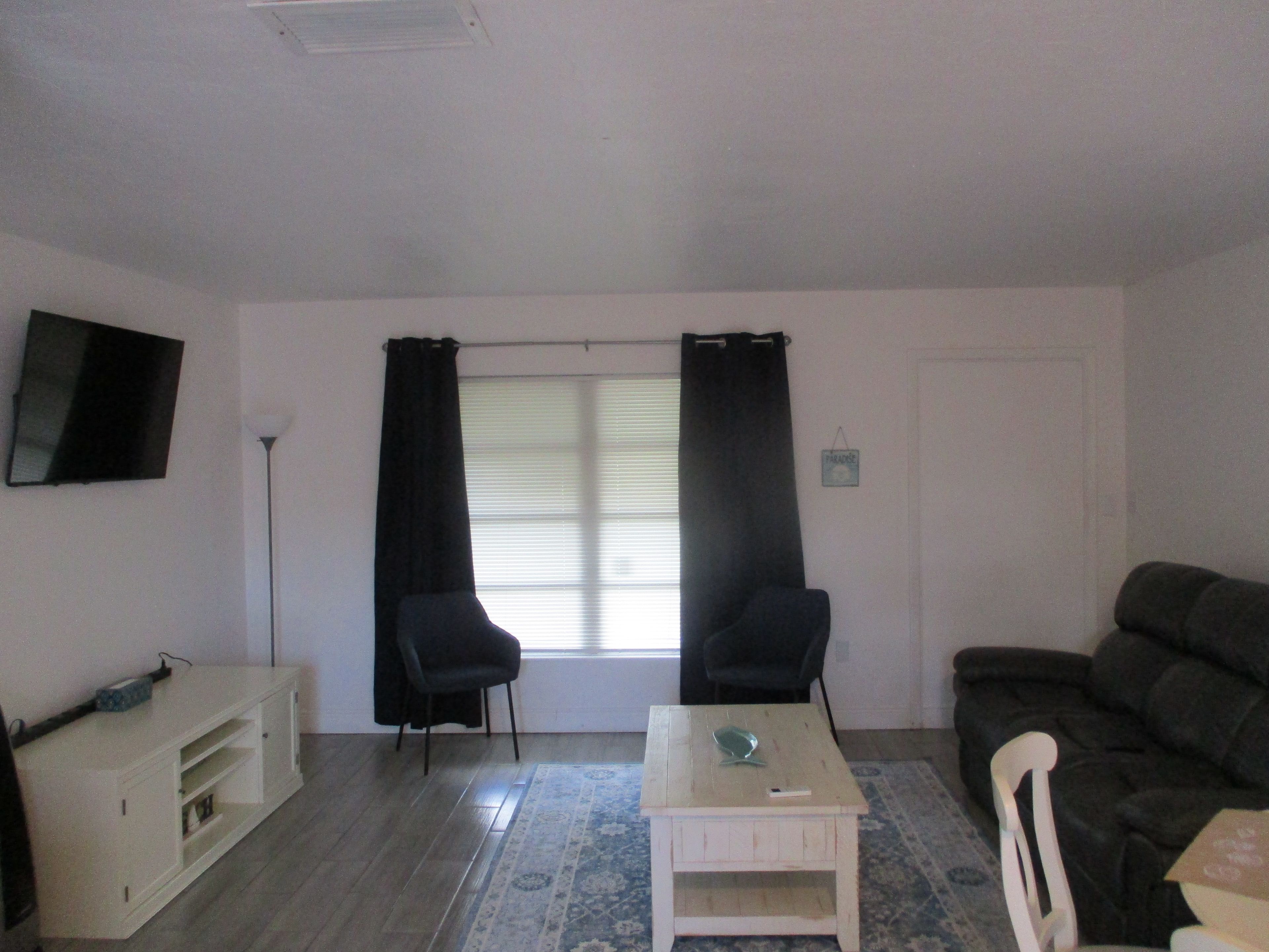 A living room with a TV mounted on the wall, a sofa, a small table, and a chair.