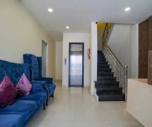 A hotel lobby with a blue sofa, a staircase, and an elevator. - Deluxe Room Day2day Hotel (Indore)