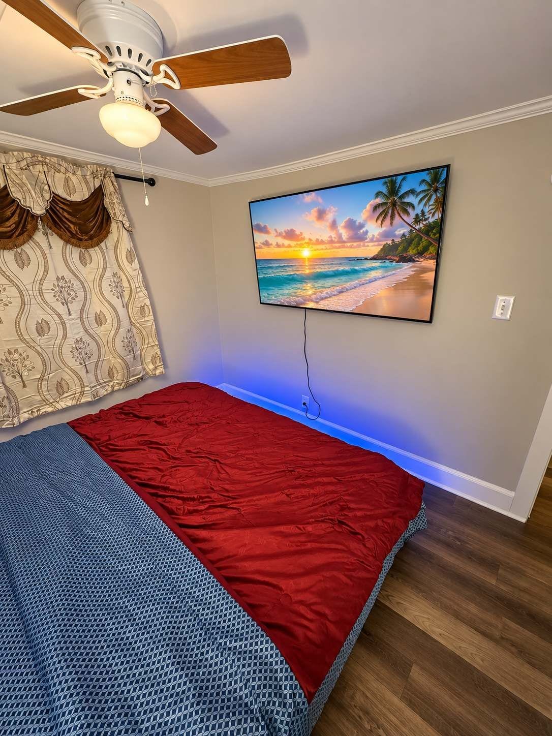 Un dormitorio con cama, ventilador de techo, televisor montado en la pared y cortina estampada.