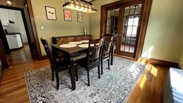 Un comedor con una mesa y sillas de madera, un tapiz estampado y una lámpara colgante.