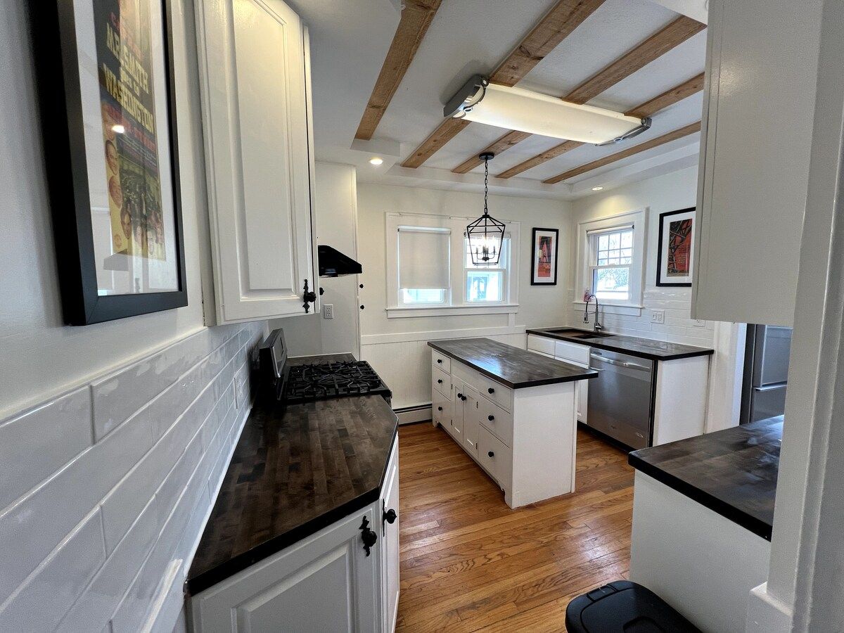 A kitchen with white cabinetry, wooden flooring, a central island, and a hanging light fixture.