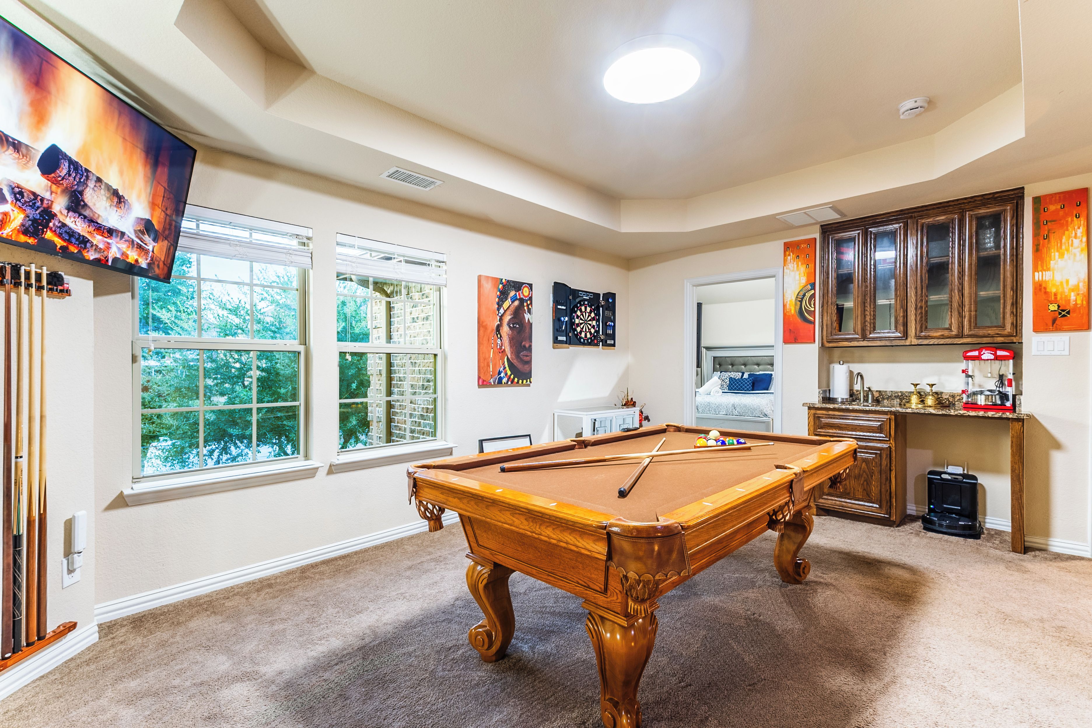 A pool table in a room with windows, a dartboard, and a television.