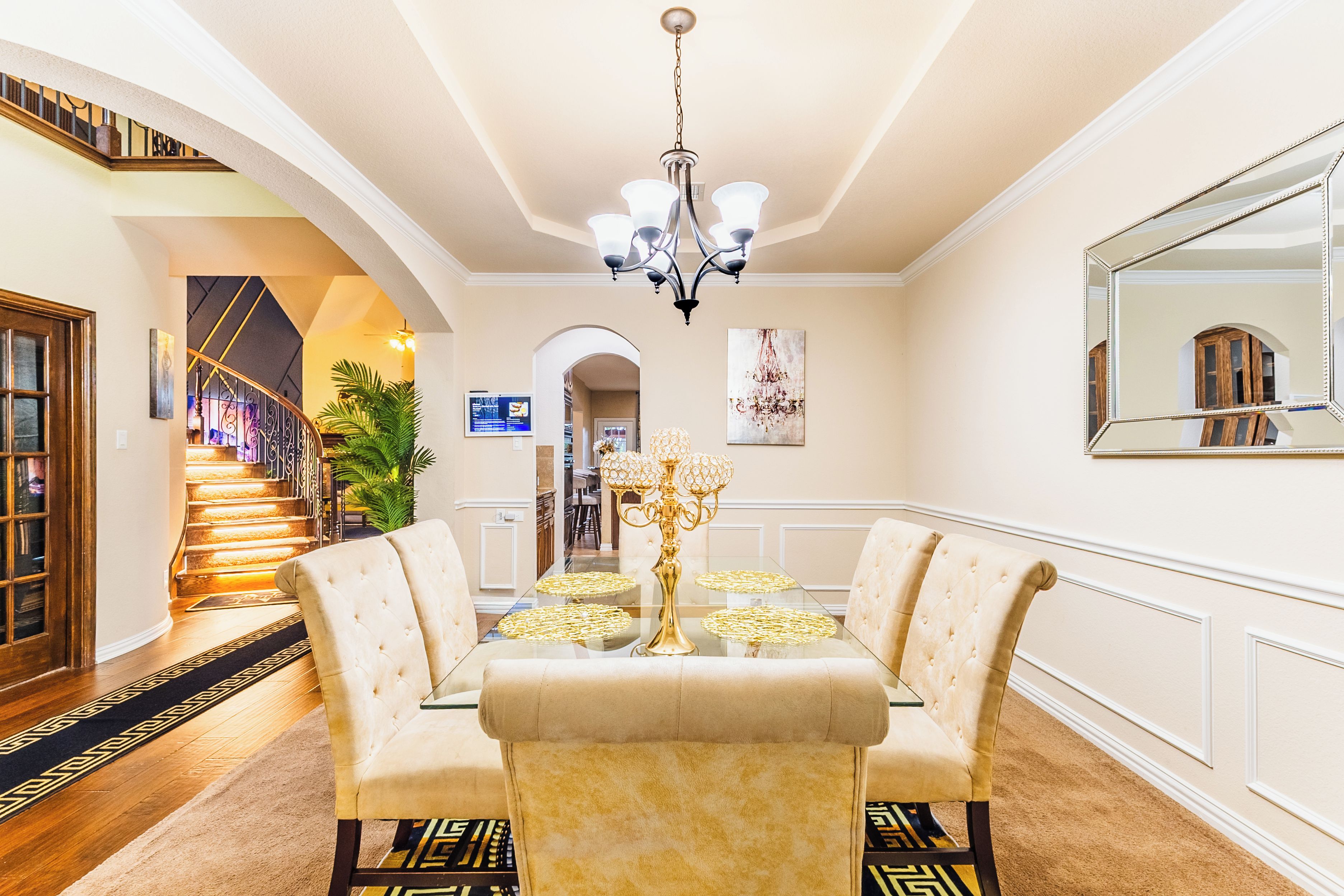 A dining area with a chandelier, a glass table, and upholstered chairs.