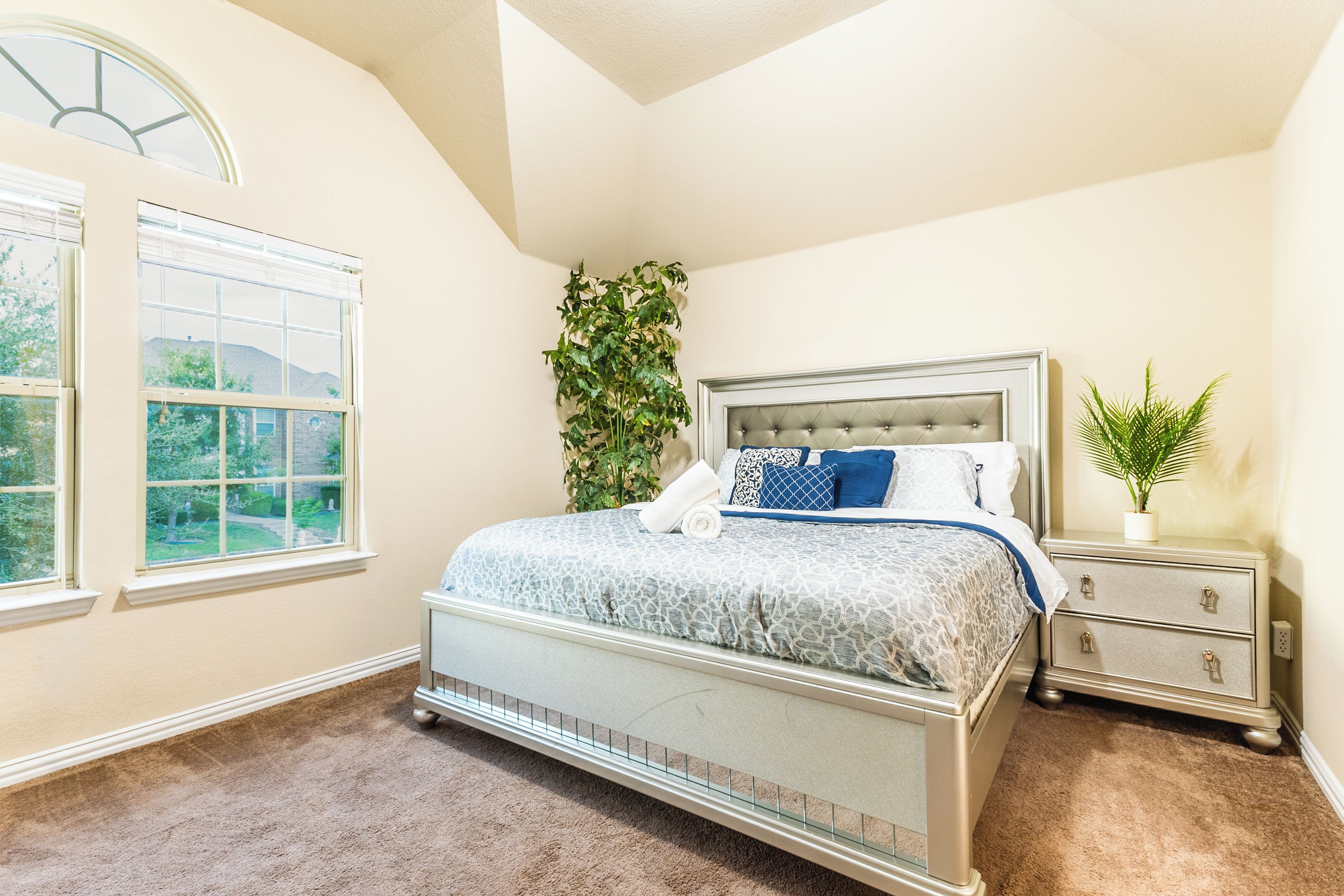 A bedroom with a bed, a nightstand, a potted plant, and a window.