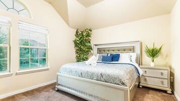 A bedroom with a bed, a nightstand, a potted plant, and a window.