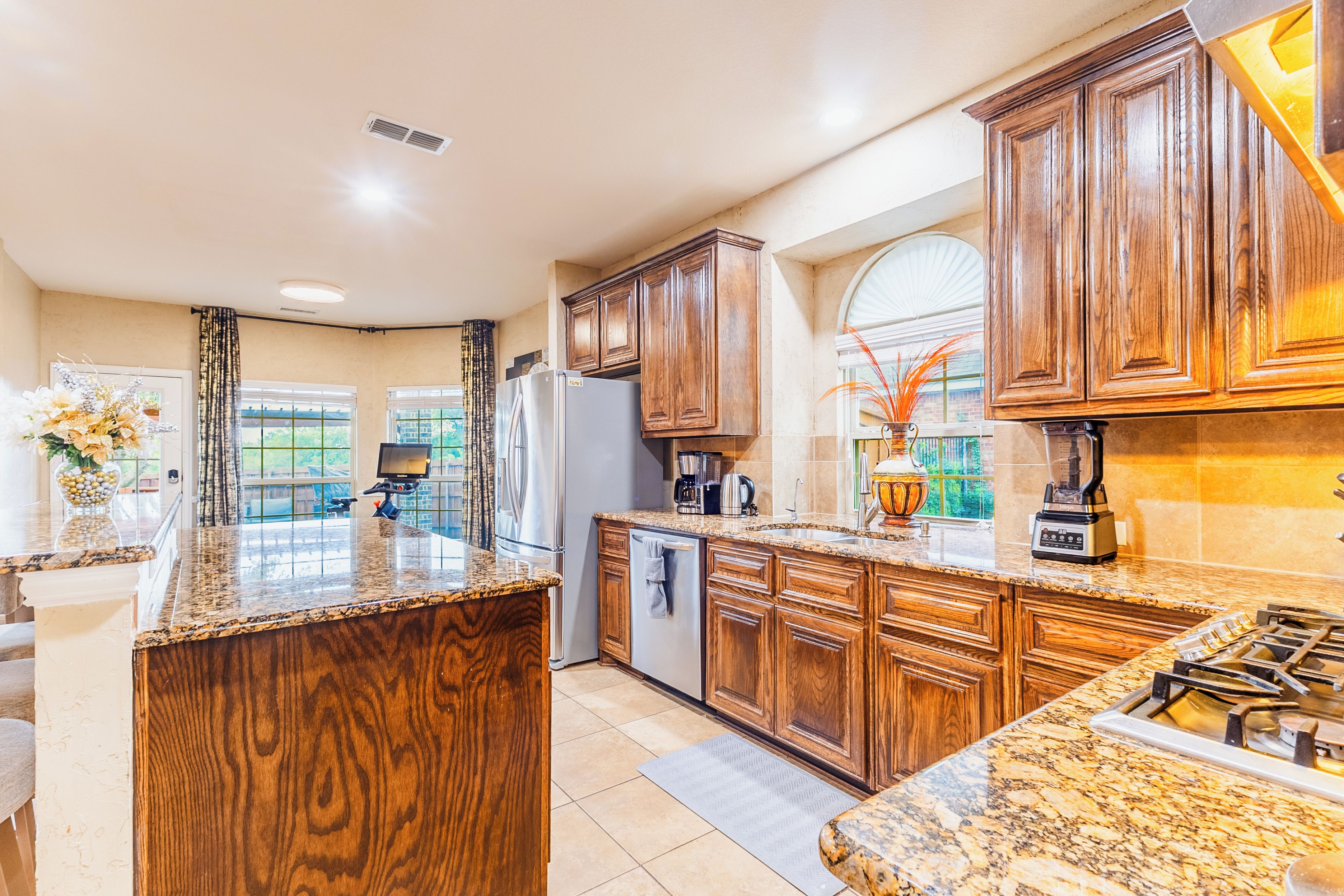 A kitchen with wooden cabinets, granite countertops, a refrigerator, a stove, and a coffee maker.