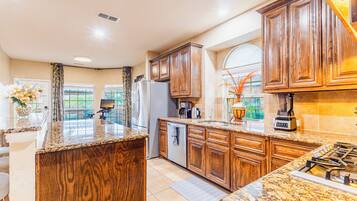 A kitchen with wooden cabinets, granite countertops, a refrigerator, a stove, and a coffee maker.