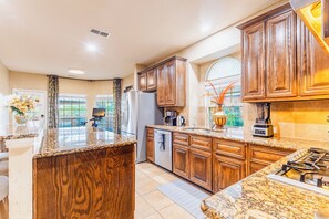 Una cocina con armarios de madera, encimeras de granito, refrigerador, estufa y cafetera.
