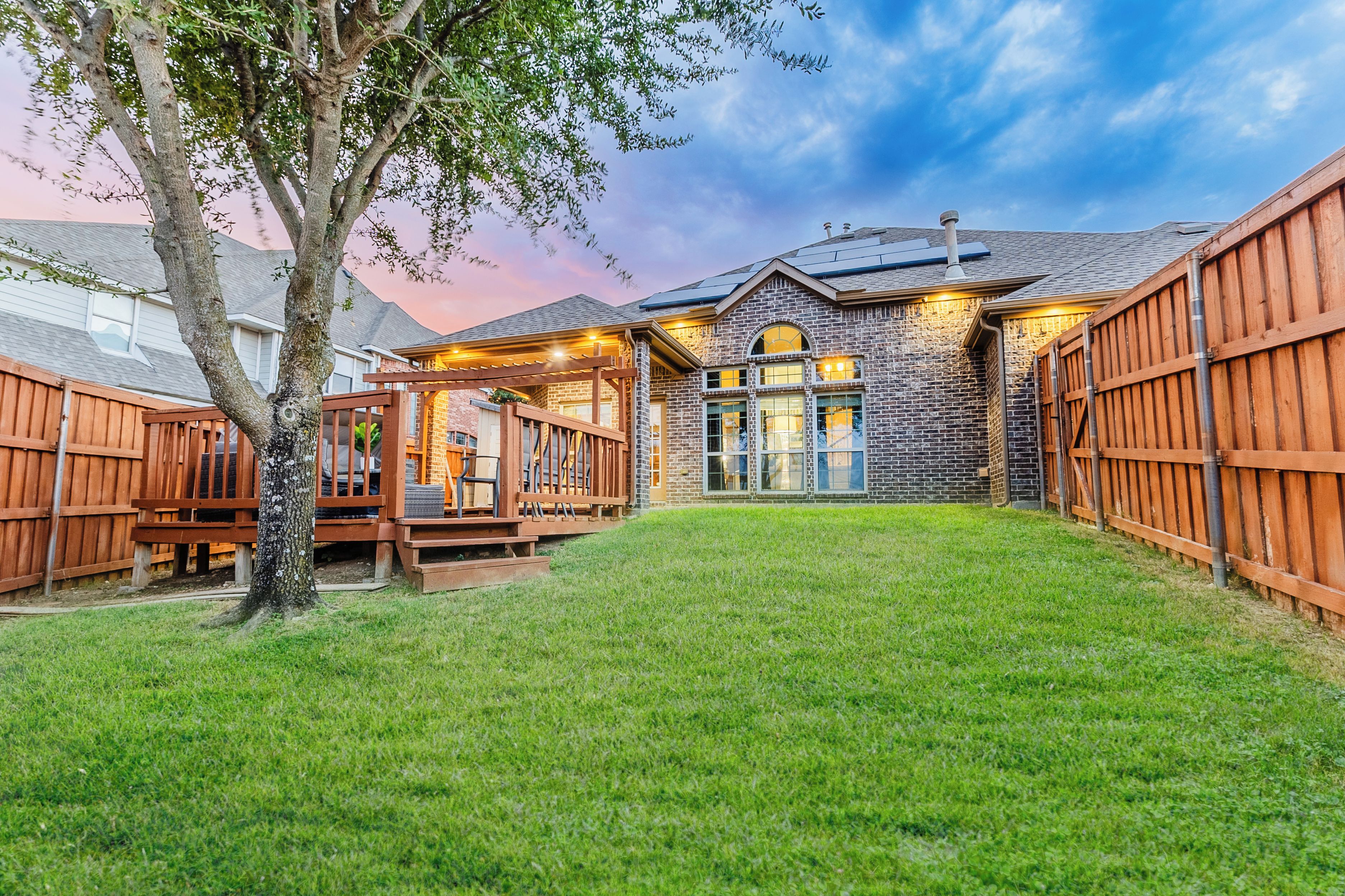 A backyard with a wooden deck, a brick house, and a well-maintained lawn.