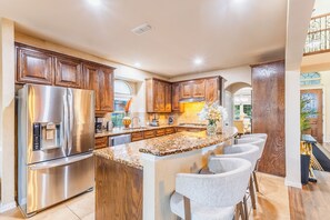 A modern kitchen with wooden cabinets, stainless steel appliances, and a central island with bar seating. - Family Retreat - Theater, Game Room + King Bed (DeSoto)