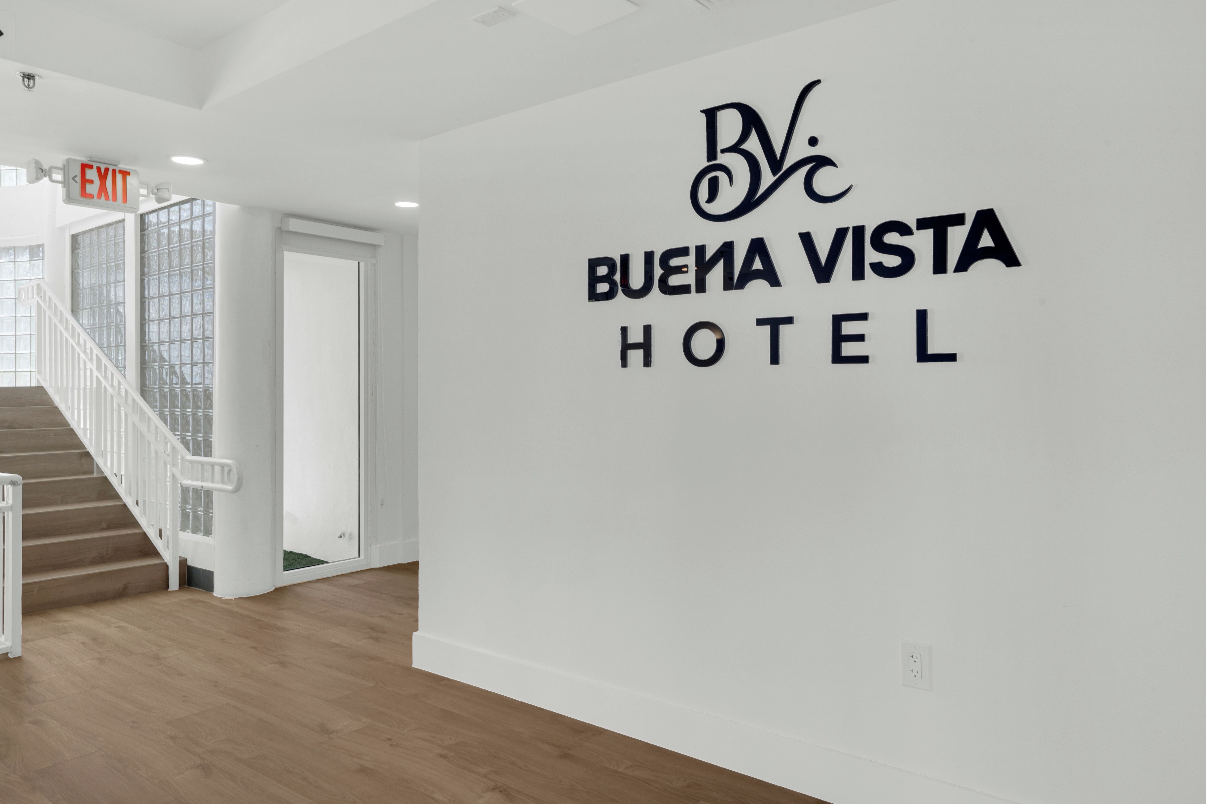 A hotel interior with a staircase, an exit sign, and a wall with the hotel's name.