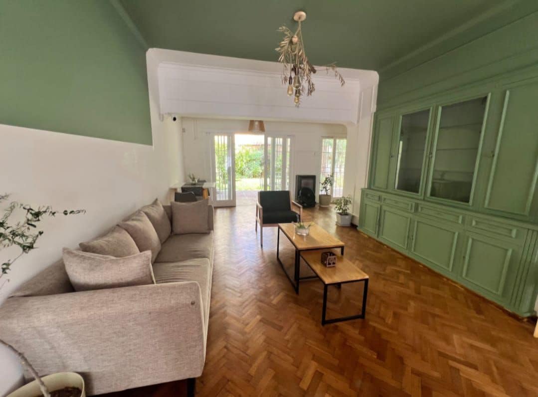 Ein geräumiges Wohnzimmer mit Fischgrätparkett, einer Sofagarnitur, einem Couchtisch und einem grünen Schrank.