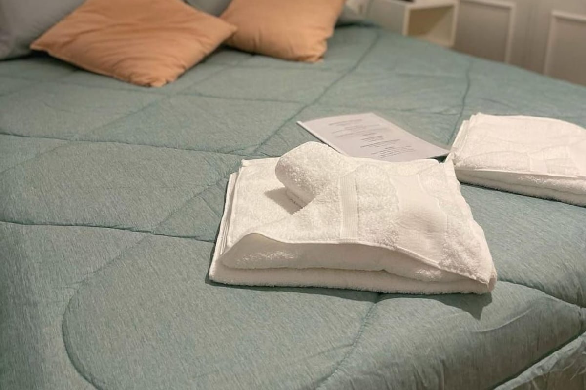 A bed with a quilted cover, two pillows, and a folded white towel on the bed.