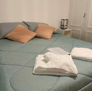 A bed with a quilted cover, two pillows, and a folded white towel on the bed. - Casa Oliva B&B (Mendoza)