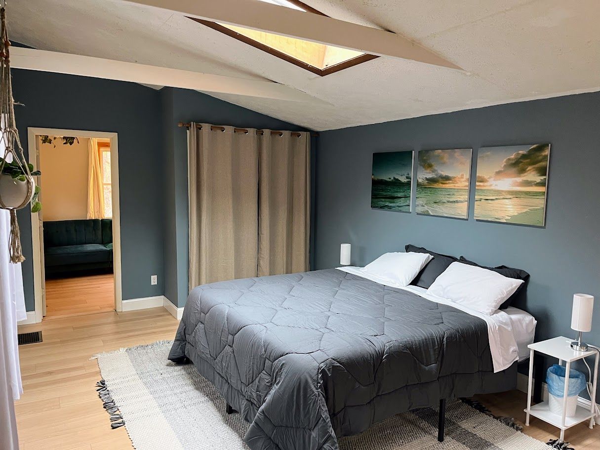 A bedroom with a large bed, a bedside table with a lamp, and a view of the outdoors through a window.
