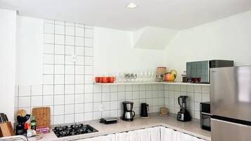 Una cocina moderna con paredes de azulejos blancos, un refrigerador de acero inoxidable y varios electrodomésticos como una cafetera y una licuadora.