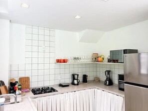 A modern kitchen with white tiled walls, a stainless steel refrigerator, and various appliances like a coffee maker and blender. - vila Anambe (Ilhéus)