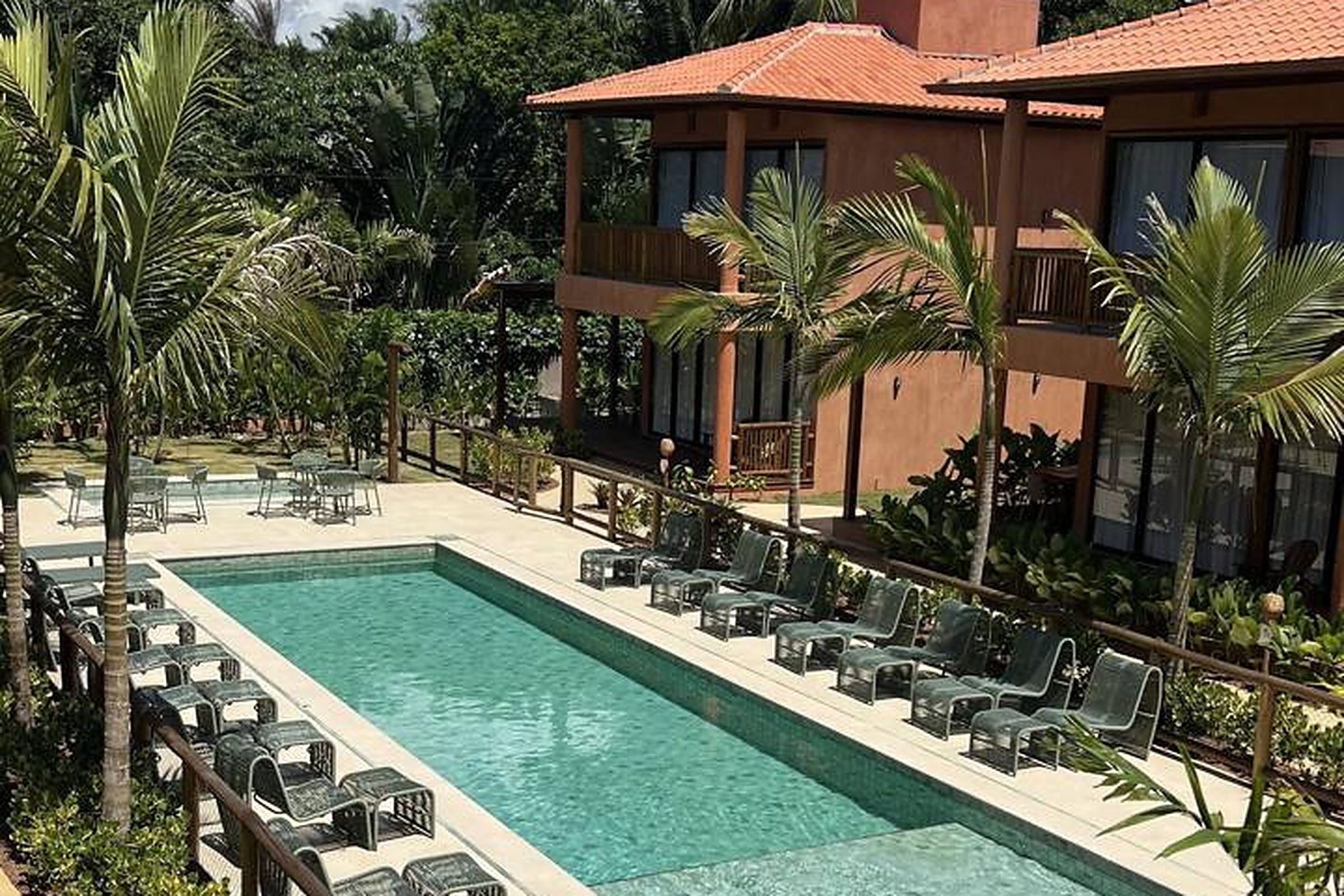 Zona de piscina con sillones de descanso y un edificio con techo rojo.