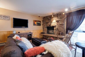 Ein Wohnzimmer mit Kamin aus Stein, einem Flachbildfernseher und einer gemütlichen Sitzecke mit Sofa und Hocker.