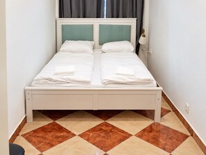 A double bed with two pillows and a folded towel, a bedside lamp, and a checkered floor pattern. - Your Vienna Routine 1BR and Living Room (Vienna)