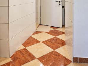 A corridor with white tiled walls and a floor with a pattern of brown and beige tiles. - Your Vienna Routine 1BR and Living Room (Vienna)