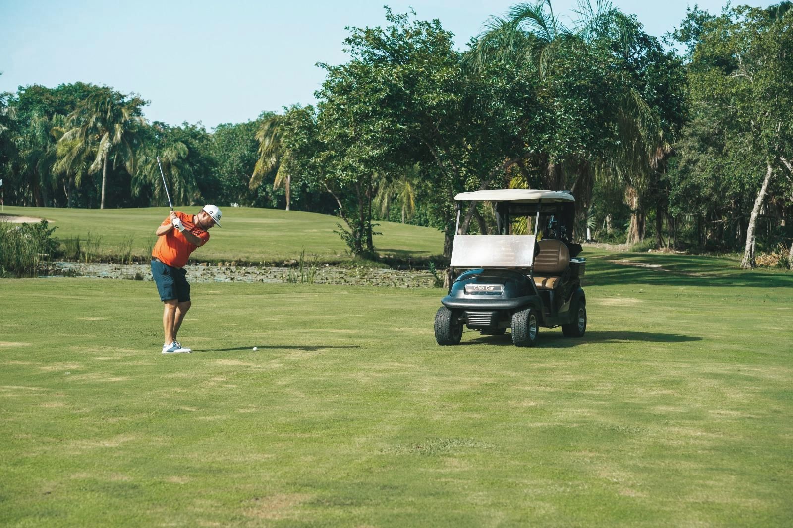 Un campo de golf con un carrito de golf y un golfista con camisa naranja.
