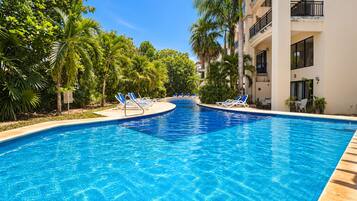 Una piscina con azulejos azules, rodeada de palmeras y sillas de descanso.