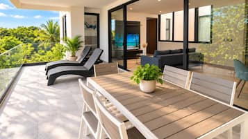 A modern outdoor seating area with a table and chairs, a sofa, and a TV screen.