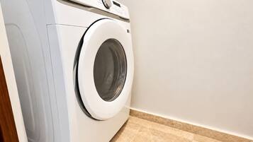 A front-loading washing machine in a laundry room with a tiled floor.