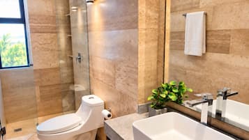 Un baño moderno con inodoro, cabina de ducha, lavamanos y un espejo grande.