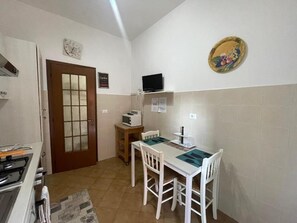 A compact kitchen with a dining table, chairs, a microwave, and a clock on the wall. - Yes Rome Holidays - One Bedroom Apartment, Sleeps 5 (Rome)