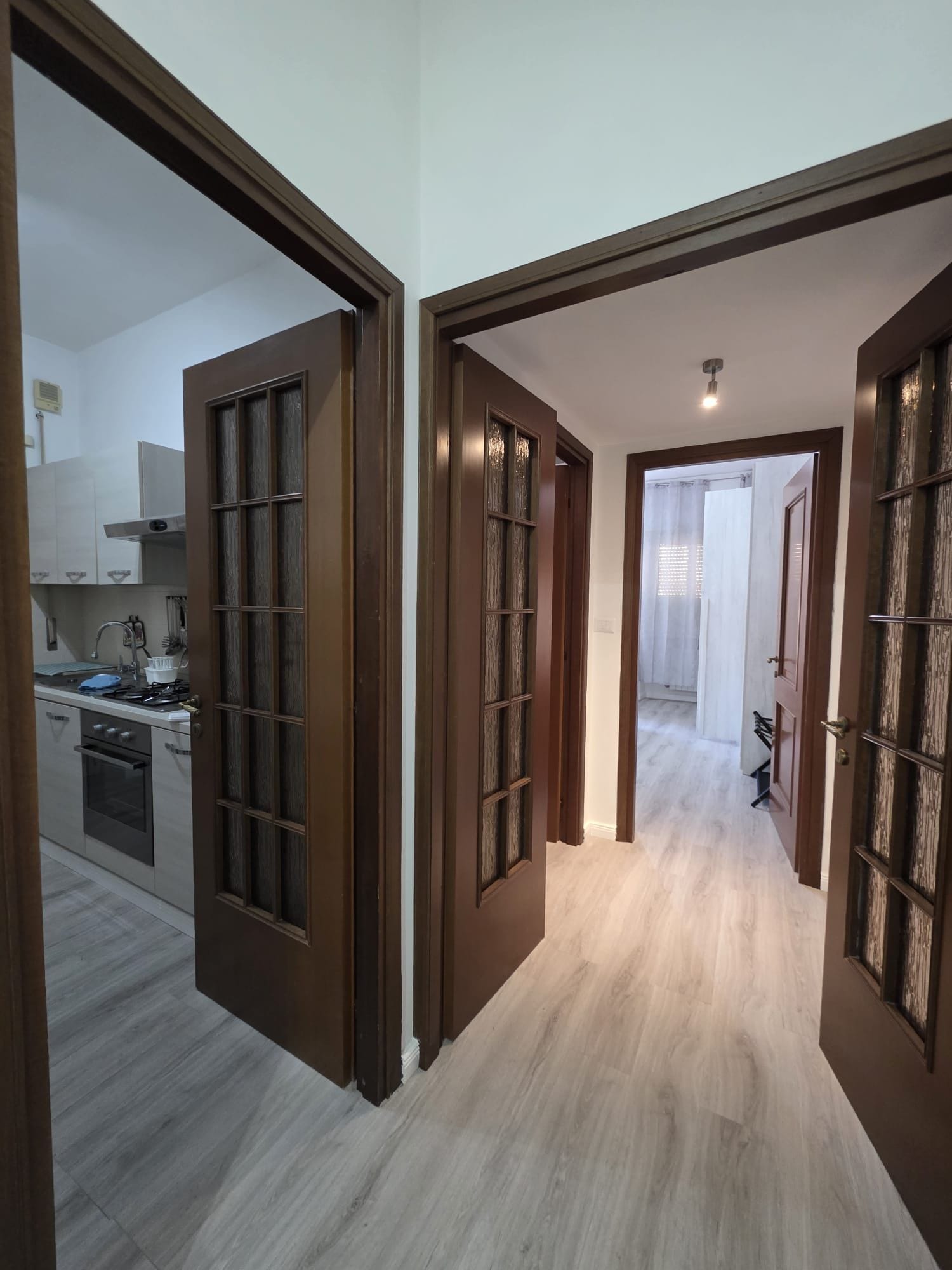 A hallway with wooden doors leading to a kitchen and a living area.
