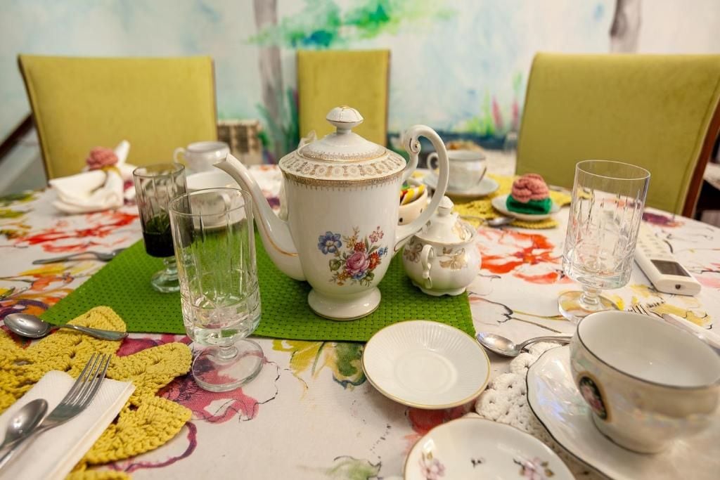 A dining table set with a floral tablecloth, a teapot, cups, and a green placemat.