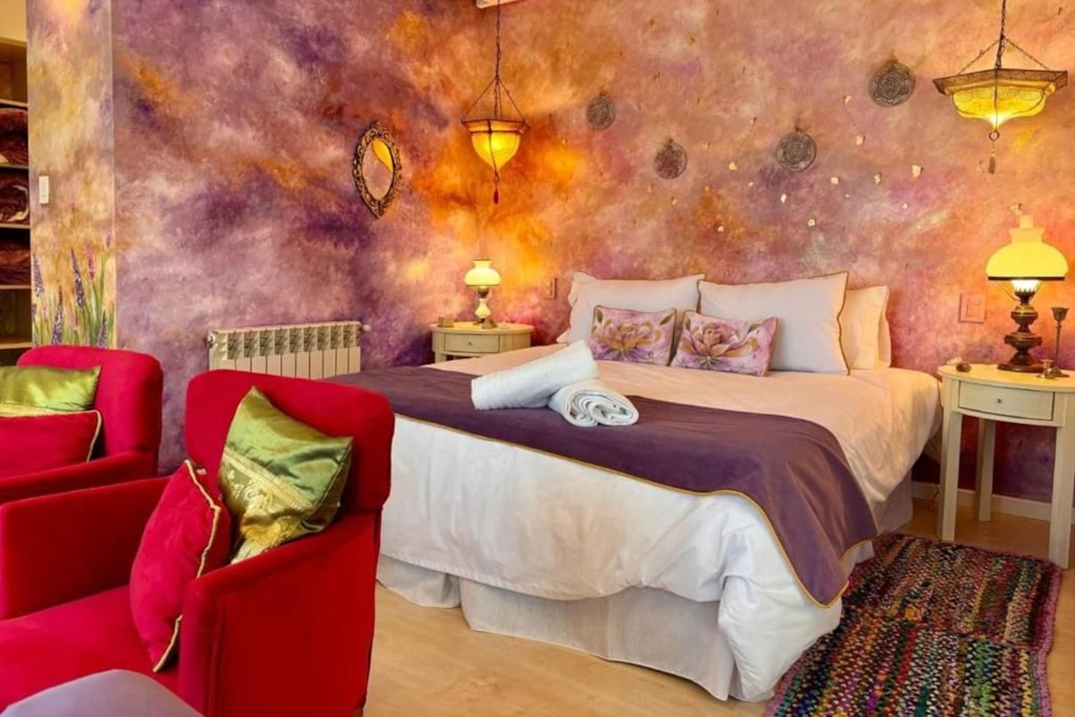 Een slaapkamer met een groot bed, twee nachtkastjes, een rode fauteuil en een kamerbreed tapijt met een patroon.