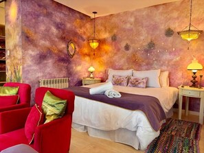 Een slaapkamer met een groot bed, twee nachtkastjes, een rode fauteuil en een kamerbreed tapijt met een patroon.