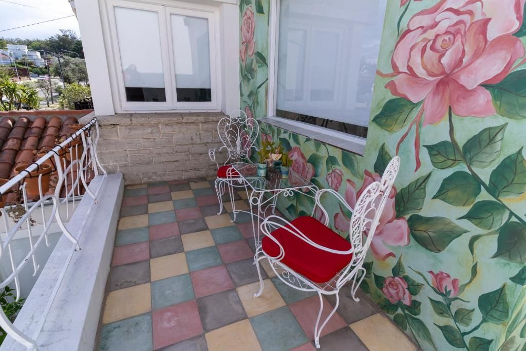 A balcony with a checkered floor, white metal chairs with red cushions, and a floral wallpaper.