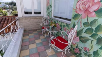 A balcony with a checkered floor, white metal chairs with red cushions, and a floral wallpaper.