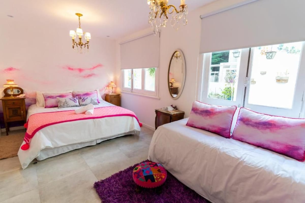 Een slaapkamer met twee bedden, een kroonluchter, een grote spiegel en een raam met uitzicht op groen.