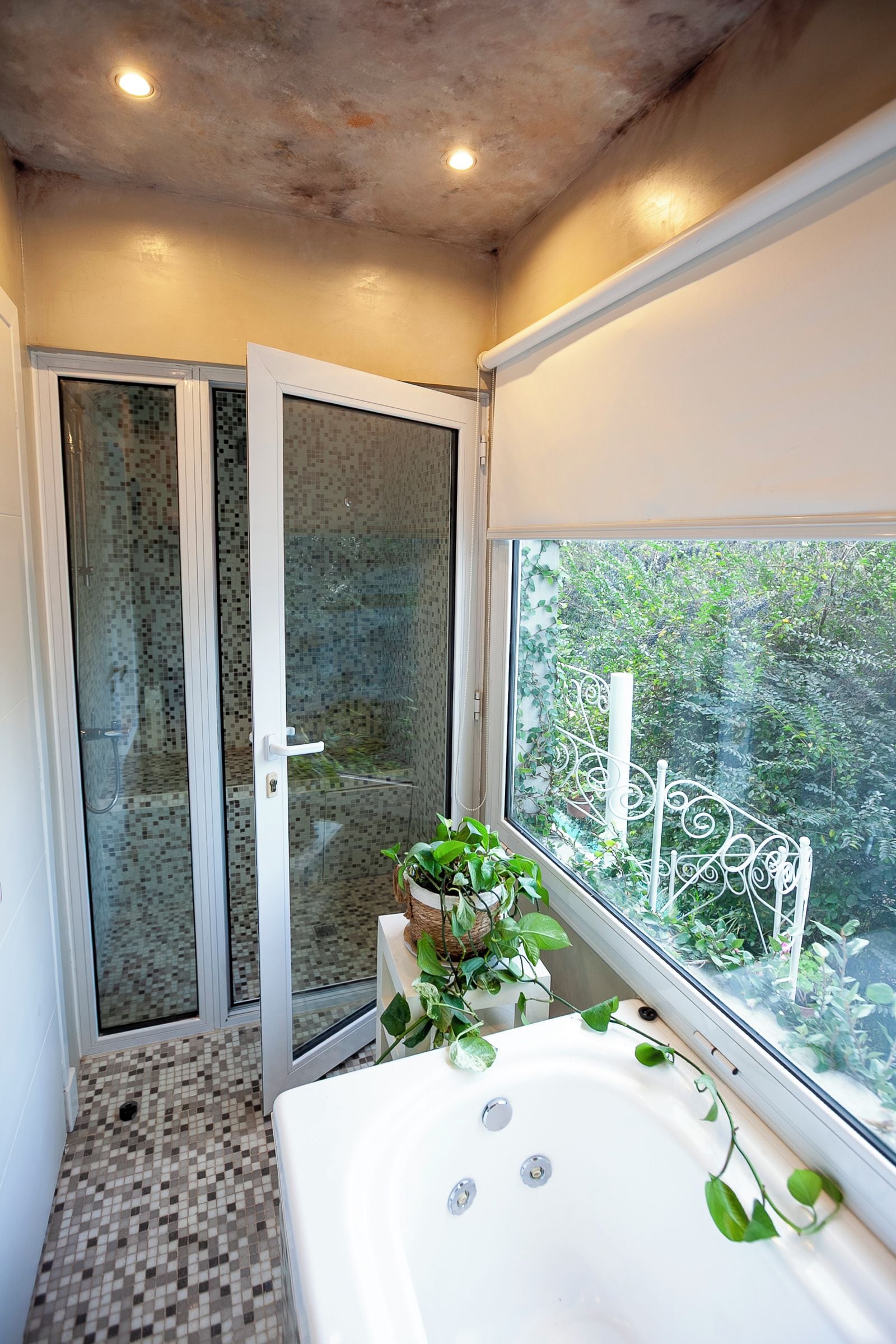 A bathroom with a shower, a bathtub, and a window with a view of greenery.
