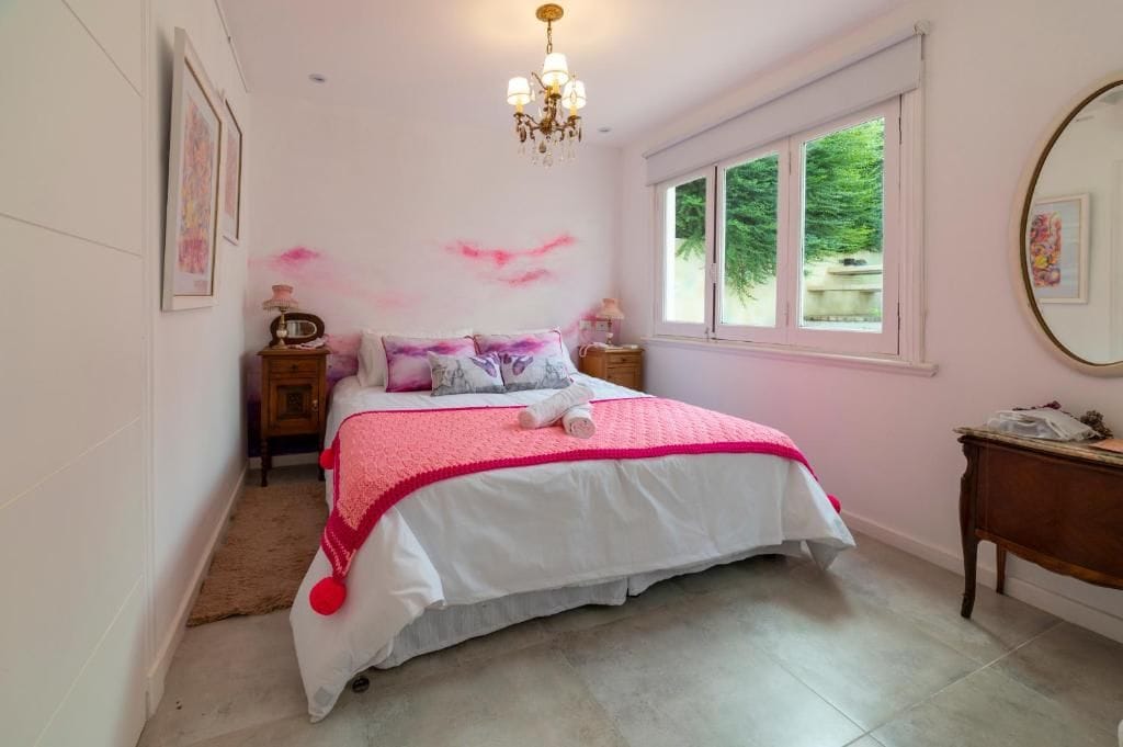 A bedroom with a bed, bedside tables, a window, and a chandelier.