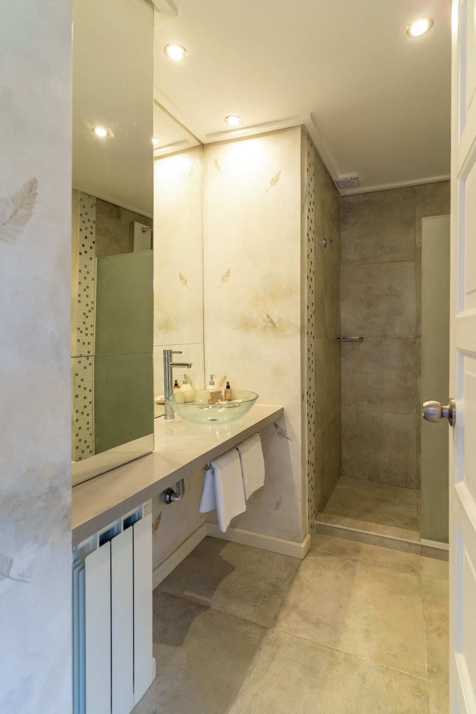Un baño con lavabo de vidrio, un espejo y una zona de ducha.