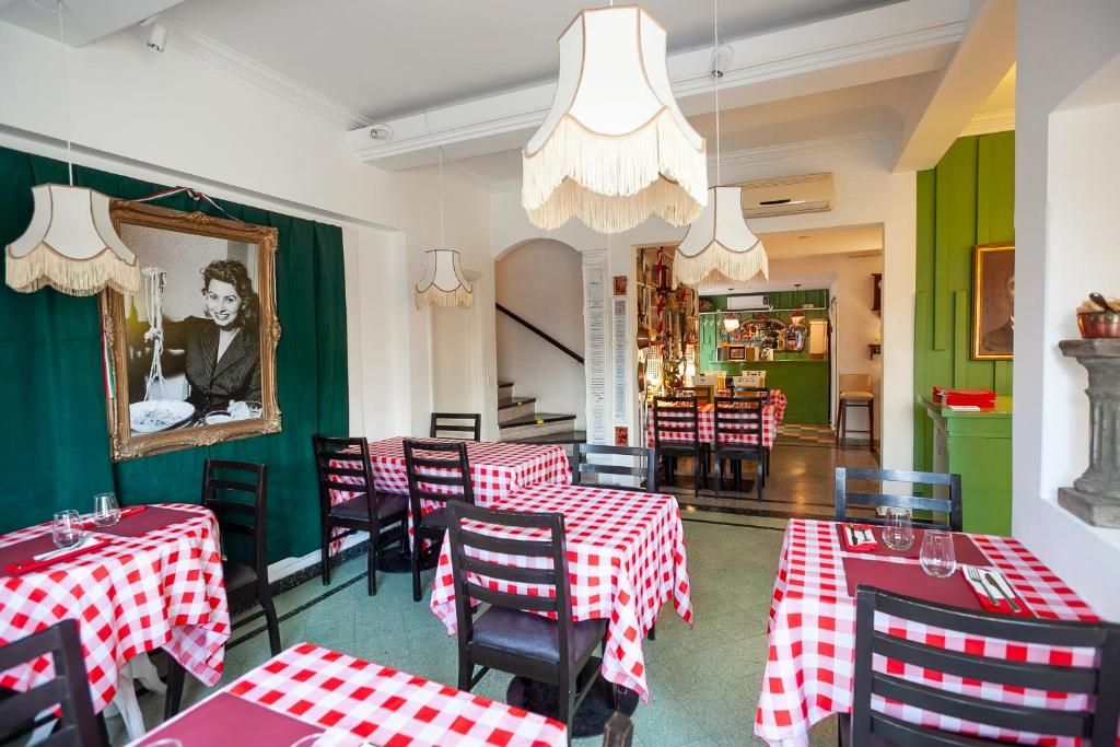 A restaurant with checkered tablecloths, hanging lamps, and a staircase leading to a bar area.