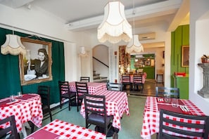Een restaurant met geruit tafelkleed, hanglampen en een trap naar een barruimte.