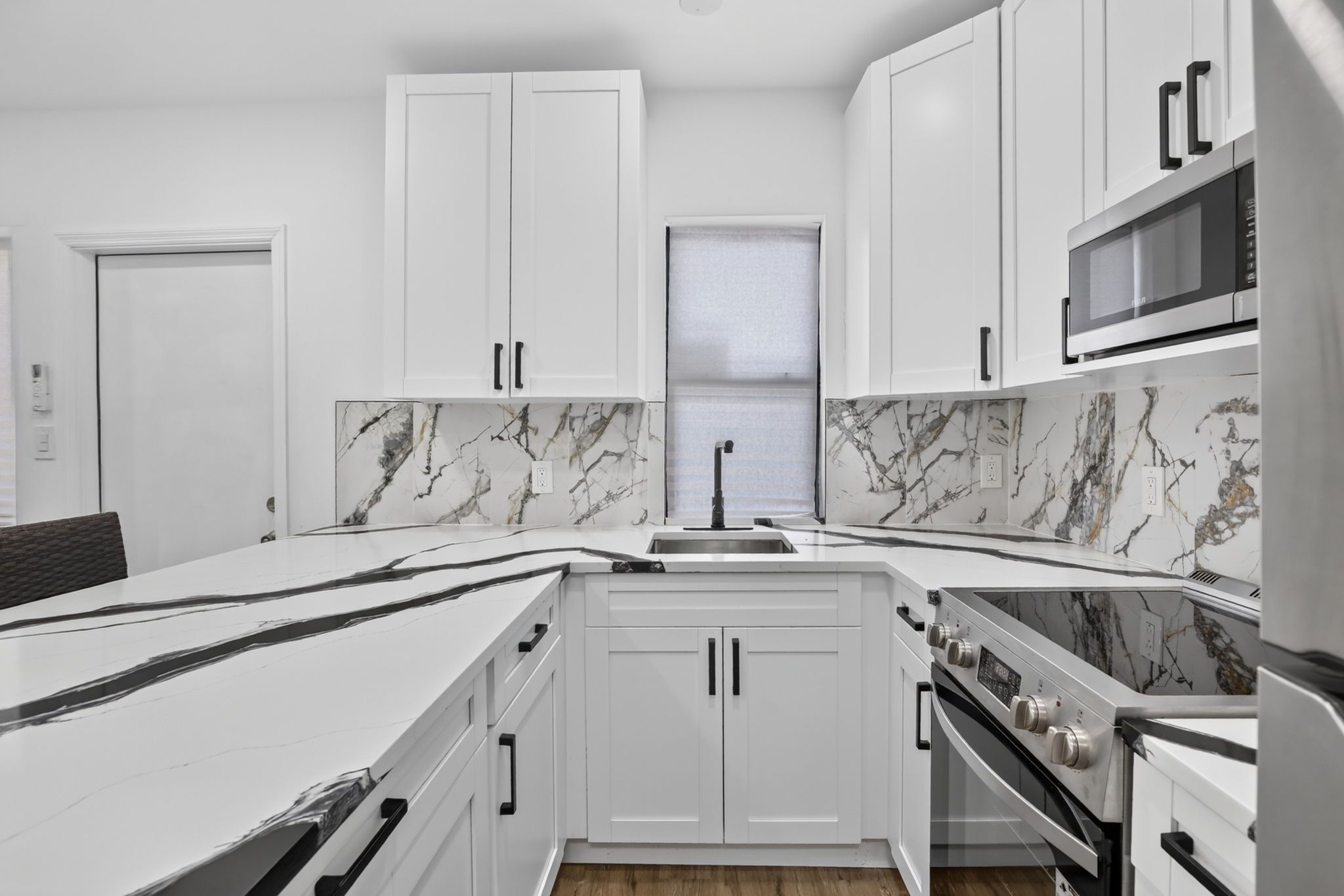 A modern kitchen with white cabinets, a marble backsplash, a built-in oven, and a microwave.