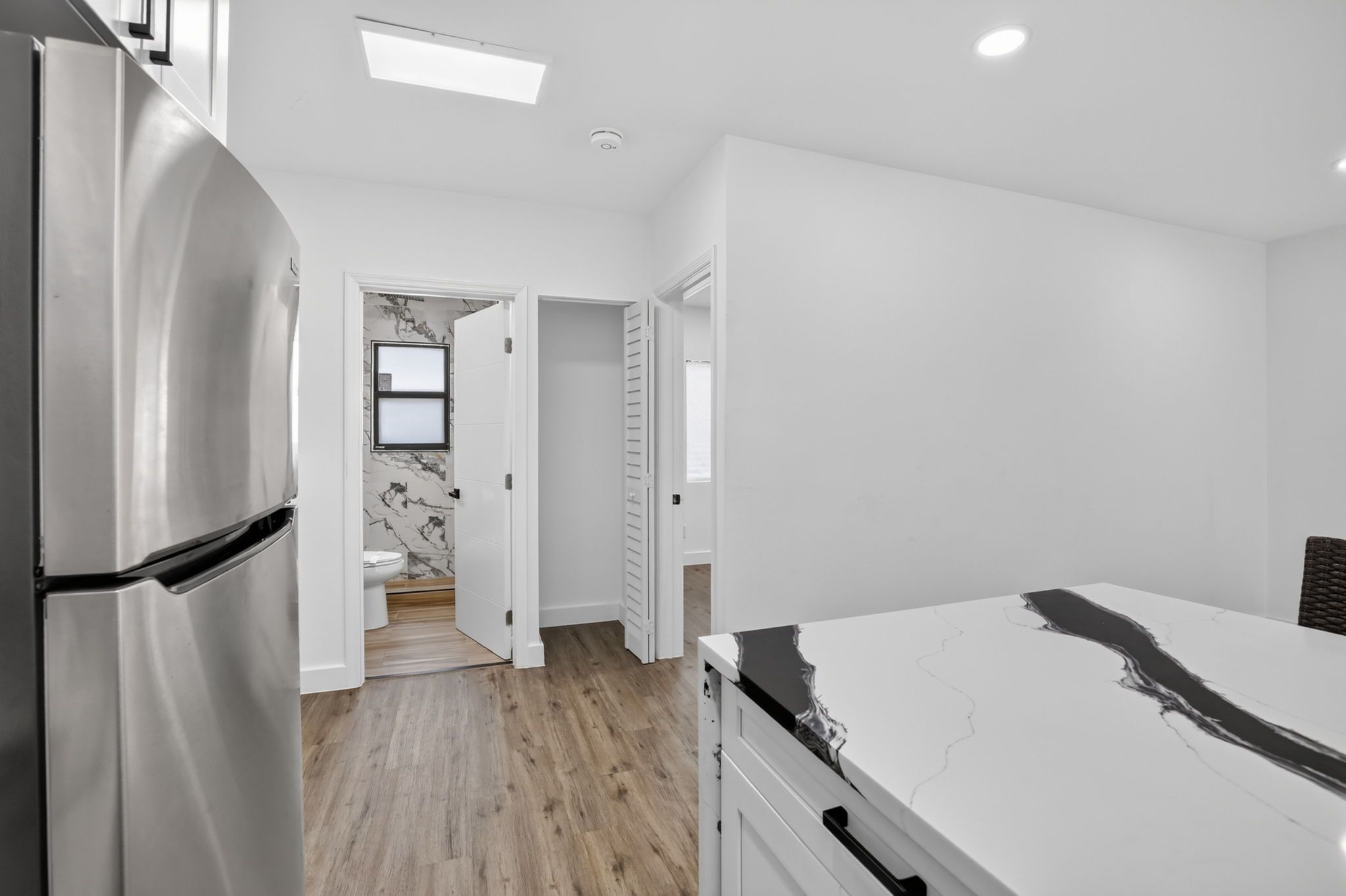 A modern kitchen with a refrigerator, a marble countertop, and a wooden floor.